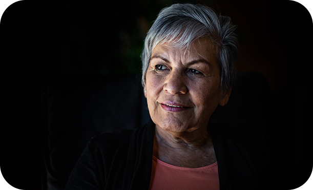 A woman with gray hair sitting in front of a black background.