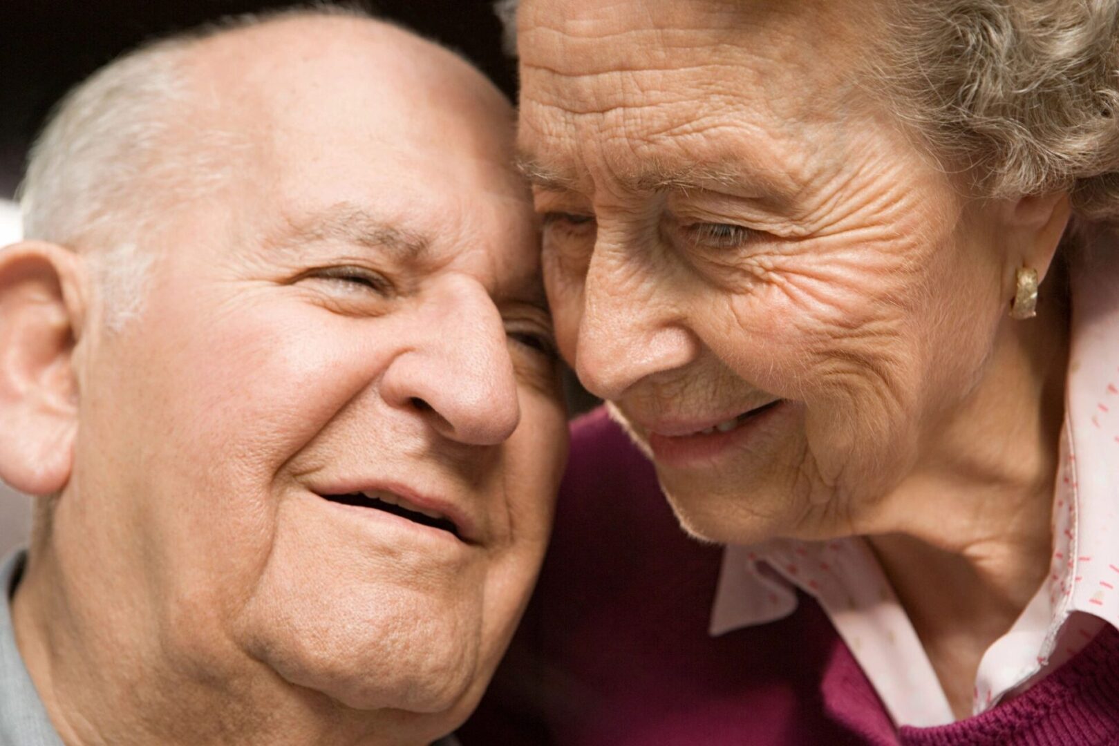 An older couple smiling at each other with their heads touching.