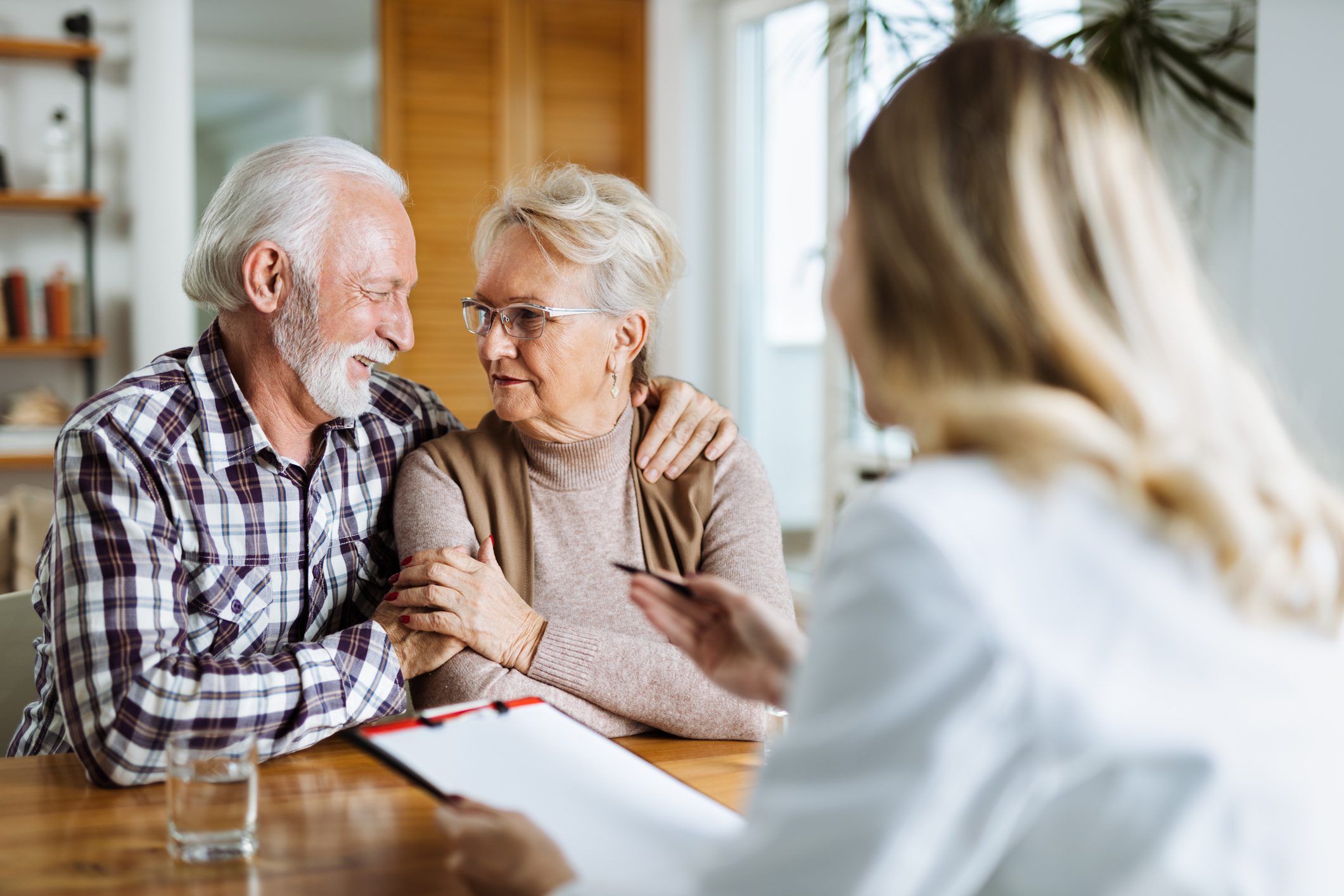 An elderly couple shares a warm moment while discussing Medicare with a healthcare professional.