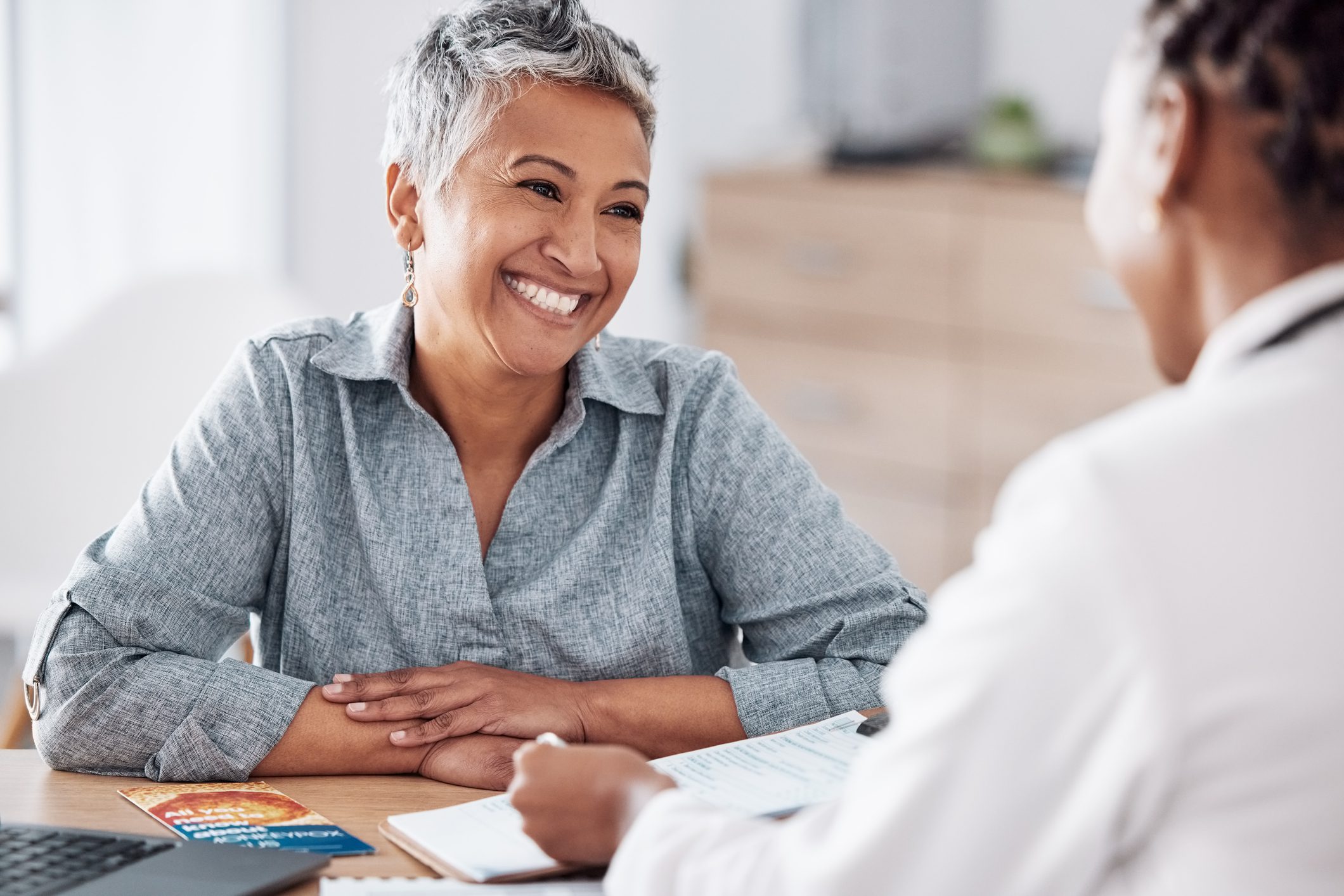 A smiling woman engages in a discussion about Medicare enrollment with a Insurance Broker at a desk.