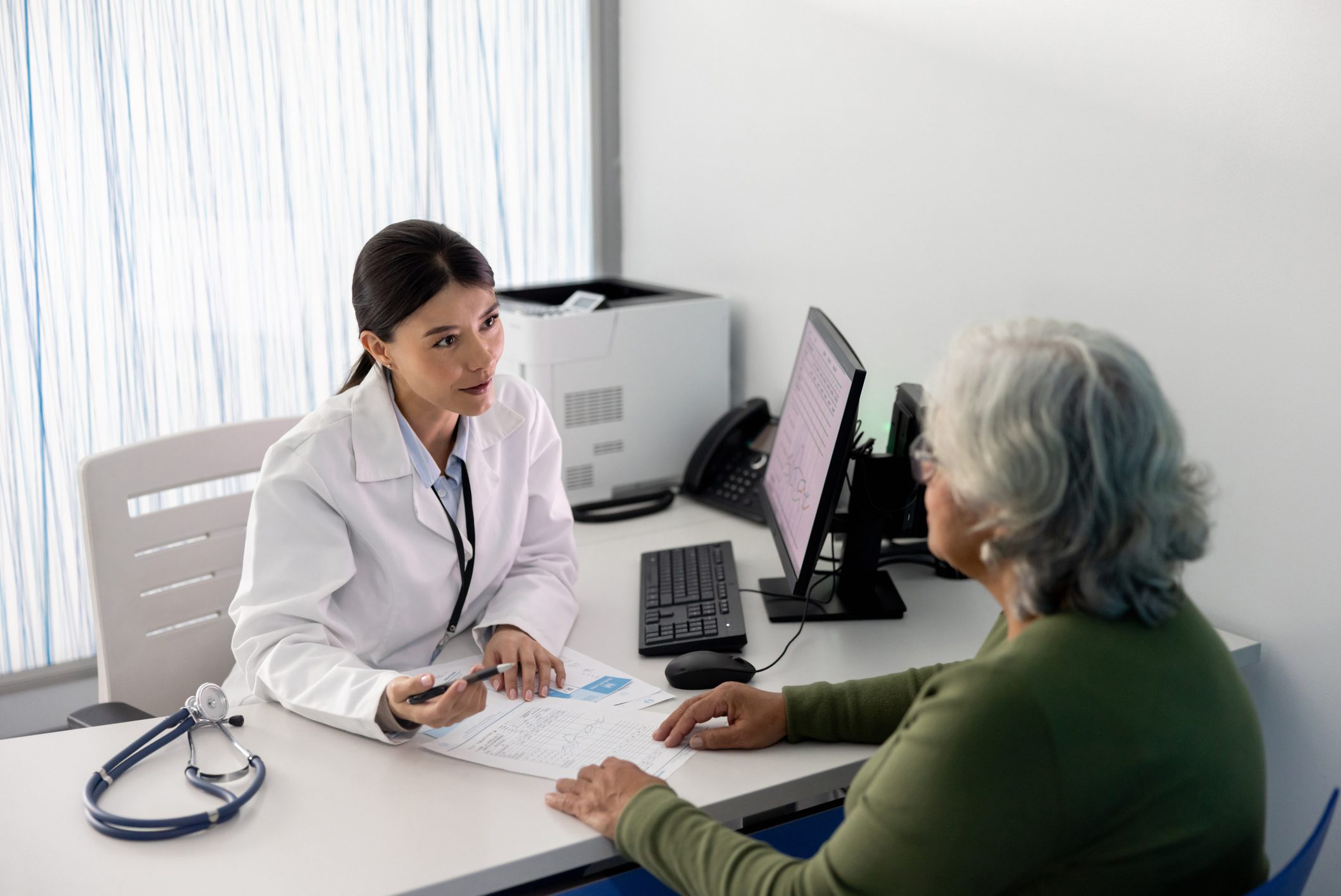 A healthcare professional discusses Medicare enrollment details with an elderly patient in a medical office.