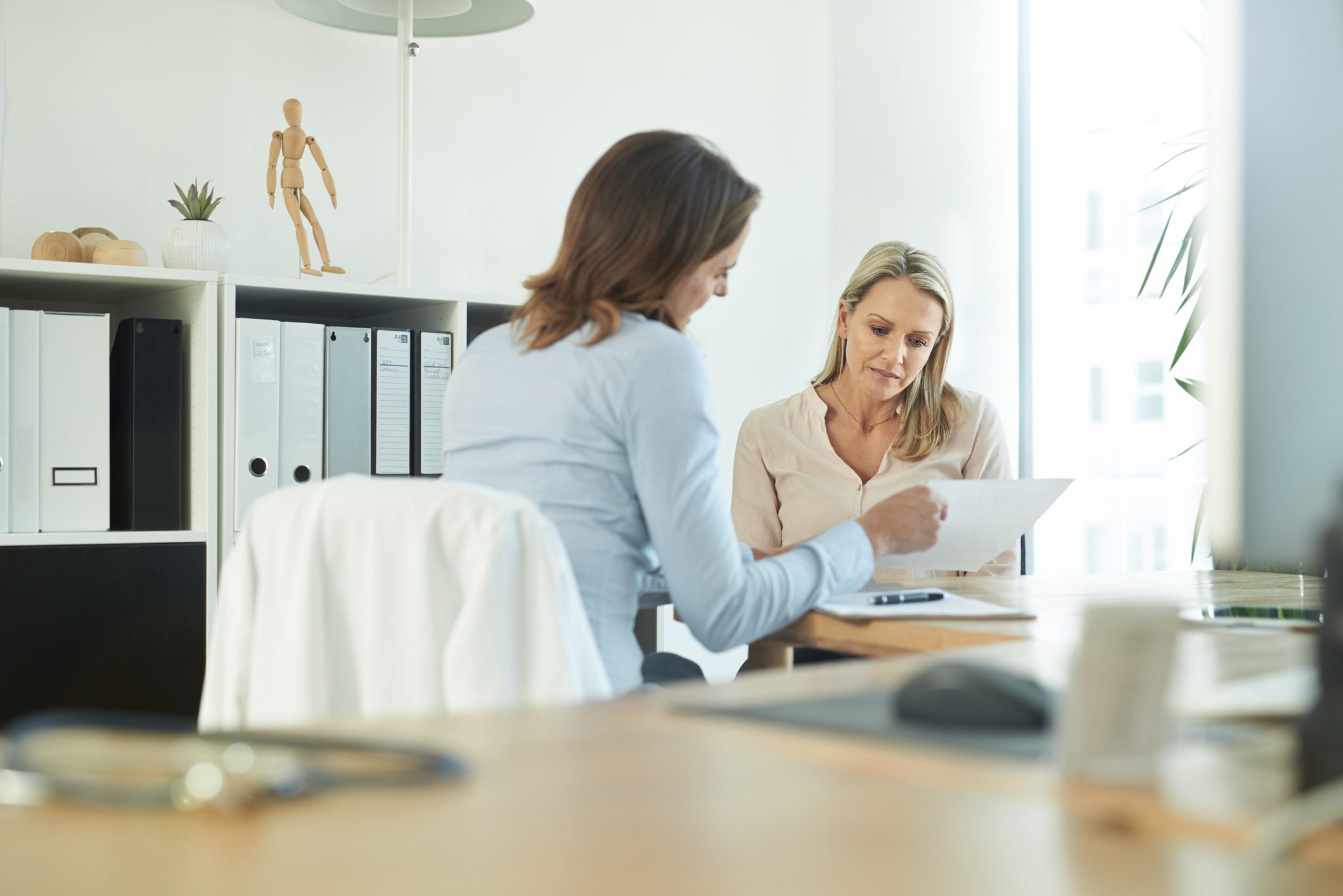 Two women discuss documents at a desk in a bright office, exploring career options for older professionals.