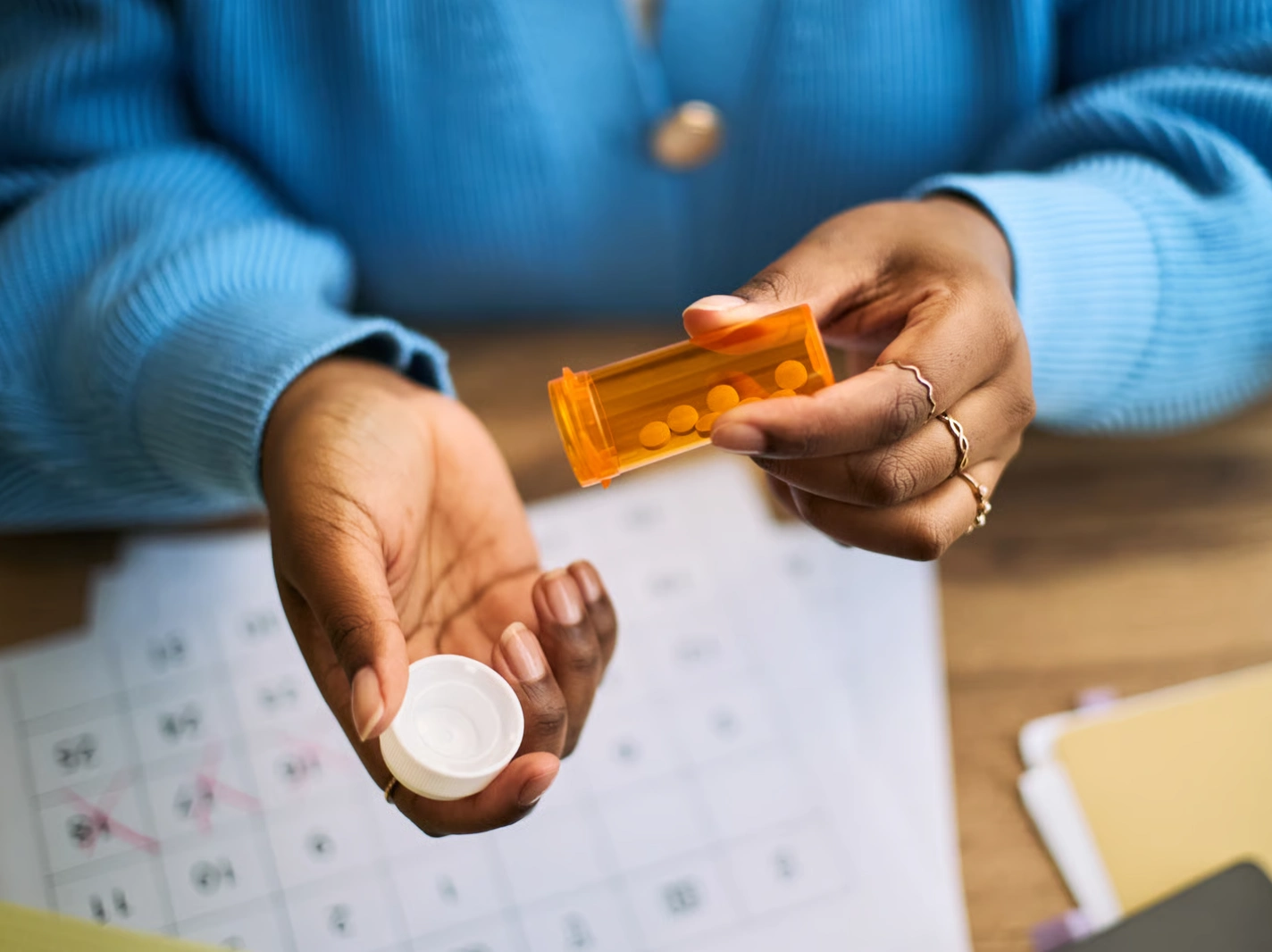 Hands holding prescription pill bottle over calendar