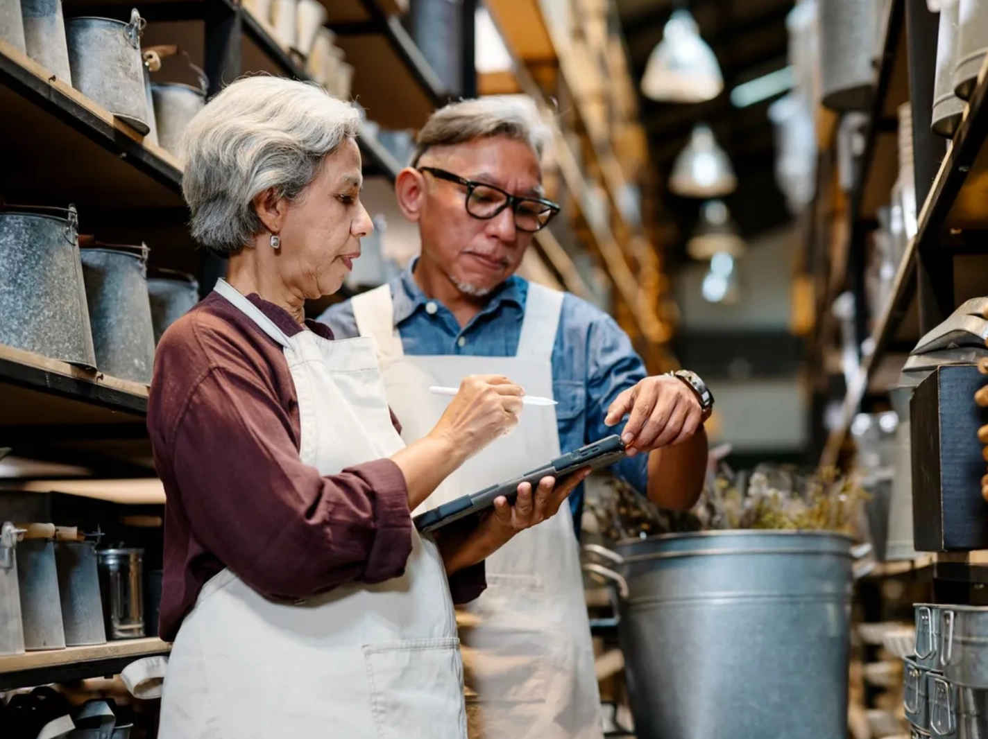 Two older workers checking tablet among metal buckets