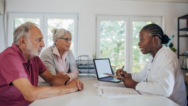A health insurance broker discusses Medicare coverage to an elderly couple in a bright, welcoming office setting.