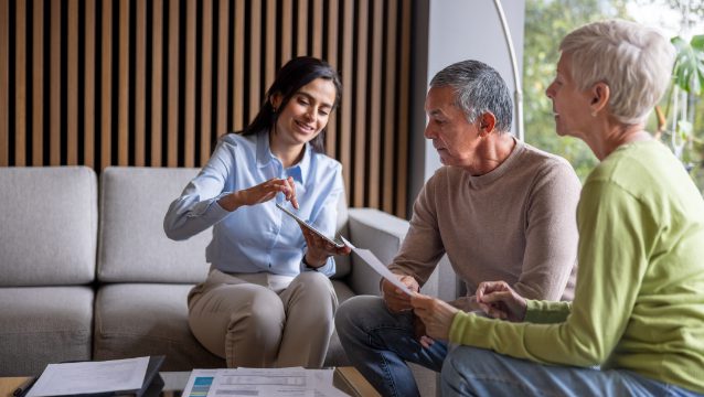 A woman explains documents to an older couple during a consultation in a modern, inviting setting.