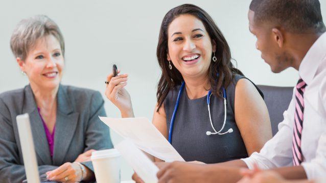A diverse group of professionals engaged in a lively discussion about Group Health Insurance, emphasizing collaboration in an office setting