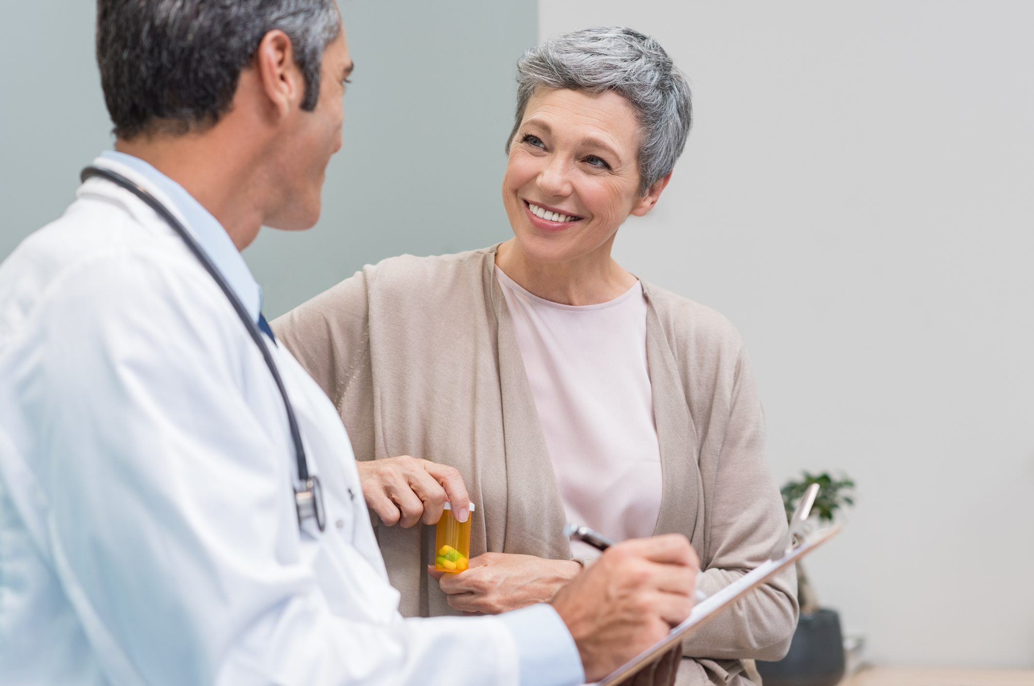Doctor consulting smiling senior woman holding prescription