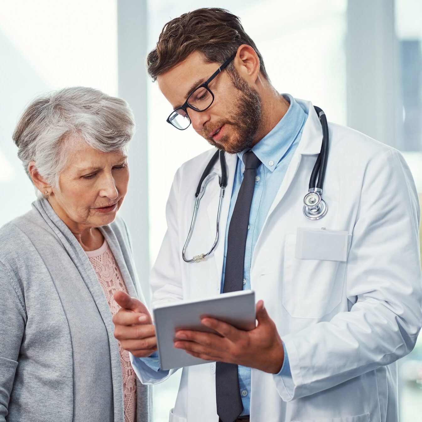 A doctor discusses Medicare options with an elderly patient while reviewing information on a tablet.